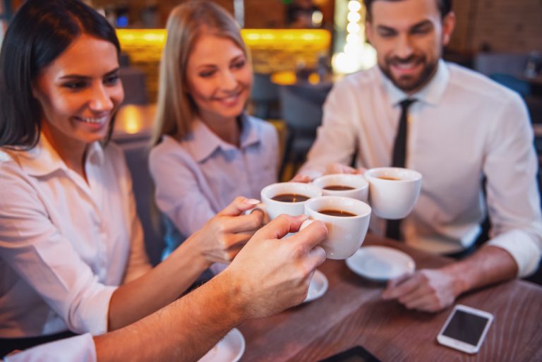 Business people clinking cups and smiling while having coffee break in cafe
